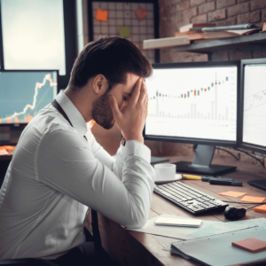 Forex trader with head in hands at his trading station