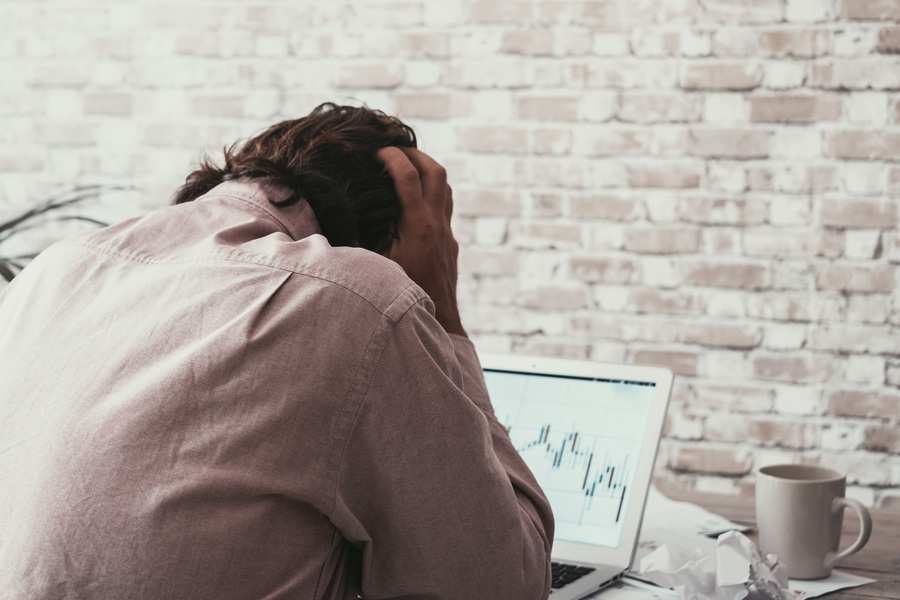 Trader with head in hands at his workstation suffering from lack of discipline