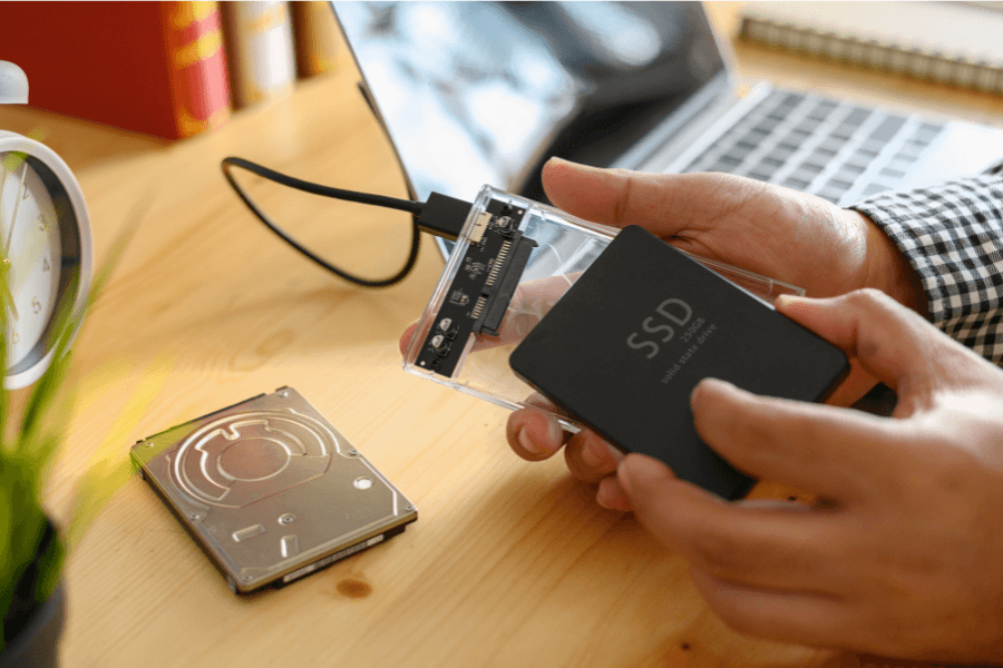 a pair of hands holding a solid state drive (SSD) with a pc in the background laid on a table