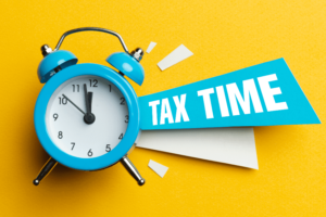 Blue clock on yellow background with Tax Time coming out the side to signify tax requirement when trading Forex